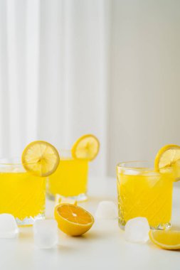 Doğal narenciye toniği ve dilimlenmiş limonlar gri arka planda buz küplerinin yanında.