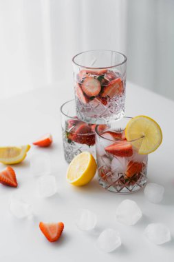 Kesilmiş limonların yanında soğuk çilekli tonik ve beyaz masanın üstünde buz küpleri olan bardaklar.