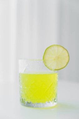 faceted glass with natural lemonade and slice of lime on grey background clipart