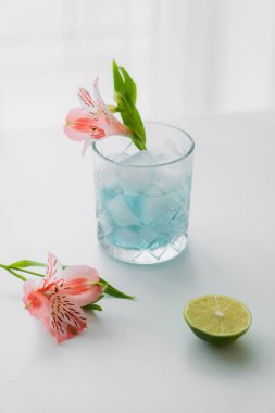 Pembe alstromerya çiçeklerinin yanında buzlu tonik su ve beyaz yüzeyde limon.