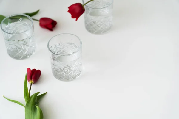 Vasos Con Patrón Facetado Agua Limpia Cerca Tulipanes Rojos Superficie — Foto de Stock