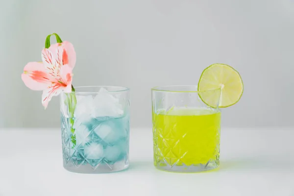 glasses of iced tonic water and lemonade with lime and tropical flower isolated on grey