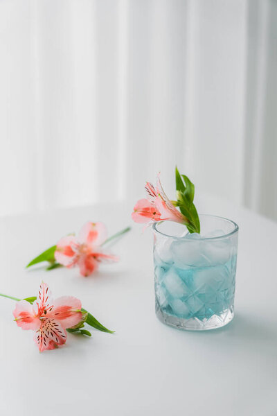 glass with cold tonic and pink alstroemeria flower on white tabletop and grey background