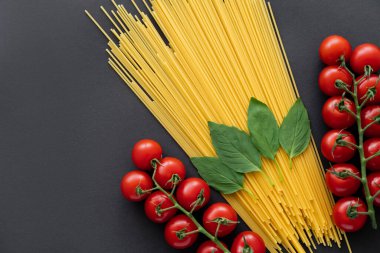 Neşeli domateslerin yanında çiğ spagetti ve siyah arka planda fesleğen. 