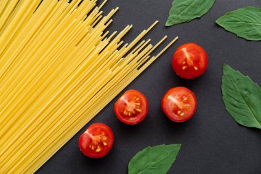 Kesilmiş kiraz domateslerinin yanında çiğ spagetti ve siyah arka planda fesleğen. 