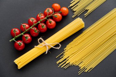 Siyah arka planda pişmemiş makarna ve kiraz domateslerinin üst görüntüsü 