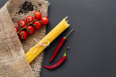 Vişne domatesleri ve kırmızı biber, siyah arka planda çuval beziyle spagetti yanında. 