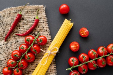 Pişmemiş spagetti ve olgun sebzelerin siyah arka plandaki çuval bezi üzerinde üst görüntüsü. 