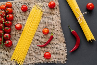 Çeri domateslerin yanında çiğ spagetti ve siyah arka planda çuval bezinde kırmızı biber. 