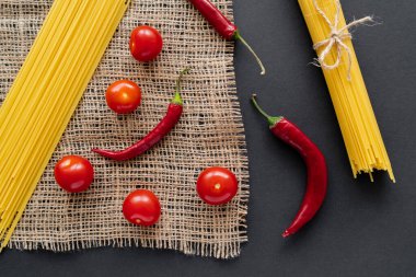 Olgun sebzelerin yanında pişmemiş spagetti, siyah arka plandaki çuval bezinin üstünde. 