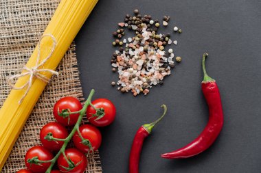Sebzelerin yanında pişmemiş spagetti ve siyah arka planda çuval bezinde tuz. 