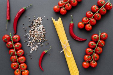 Kırmızı sebzelerin yanında çiğ makarna ve siyah arkaplanda baharatlar. 