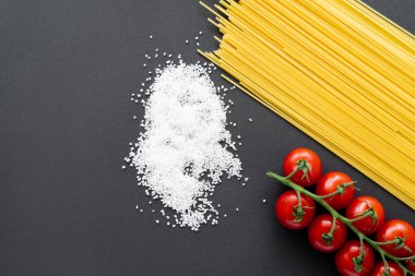 Siyah zemin üzerinde çiğ makarna ve kiraz domateslerinin yanındaki tuz manzarası 