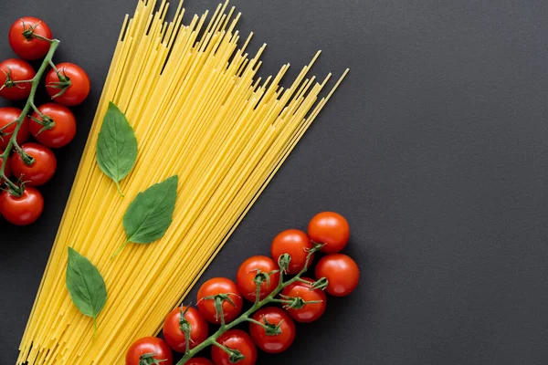 Çeri domateslerin yanında çiğ spagetti ve siyah arka planda fesleğen. 