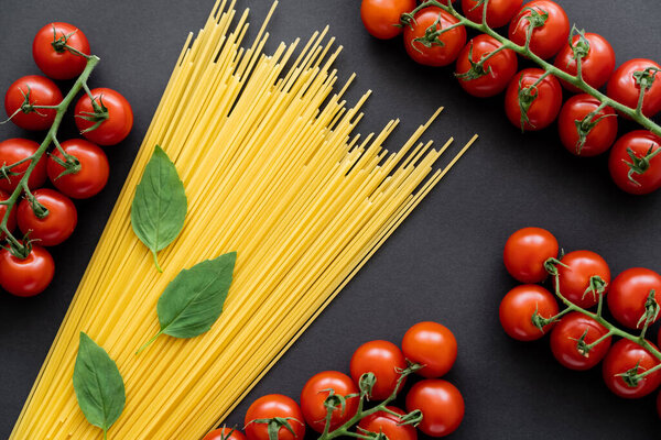 Top view of raw pasta with basil and cherry tomatoes on black background 