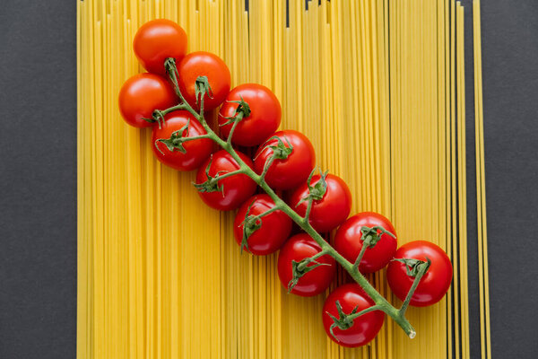 Top view of organic cherry tomatoes on raw pasta on black background 