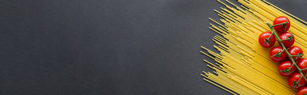 Top view of cherry tomatoes on branch on uncooked pasta on black background, banner 