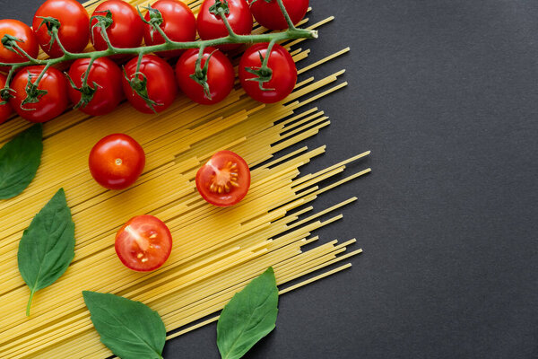 Top view of organic tomatoes and basil on raw spaghetti on black background 