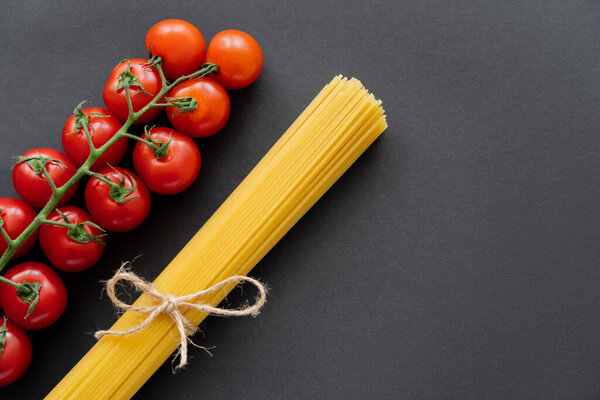Top view of raw pasta and cherry tomatoes on black background 