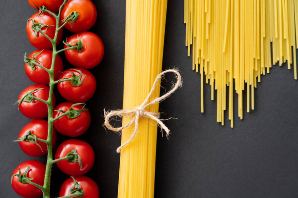 Top view of raw spaghetti and cherry tomatoes on black background 