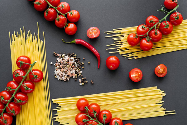 Flat lay of natural vegetables and spaghetti with spices on black background 