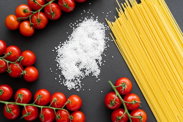 Pişmemiş spagetti ve vişneli domateslerin yanında siyah arkaplanda tuz manzarası. 