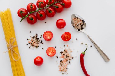 Sebzelerin yanında kaşığın içindeki baharatların ve beyaz arka planda pişmemiş makarnanın en üst görüntüsü. 