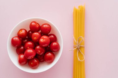 Taze vişneli domates ve pembe yüzeyde pişmemiş spagetti manzarası.