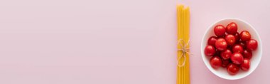 Pembe yüzeyde çiğ spagetti ve kiraz domateslerinin üst görüntüsü, afiş. 