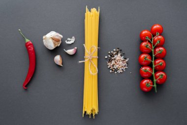 Olgun sebze ve sarımsak, pişmemiş spagetti ve siyah yüzeyde baharatlar. 