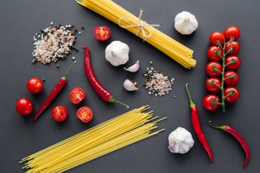 Sebze yakınındaki baharatlar ve siyah yüzeyde pişmemiş makarna manzarası. 