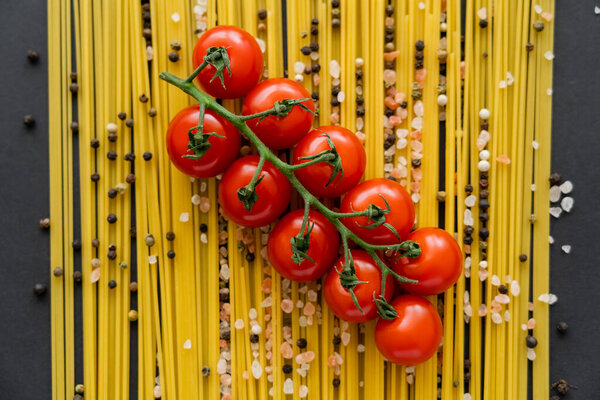 Top view of natural cherry tomatoes on blurred raw spaghetti and spices on black background 