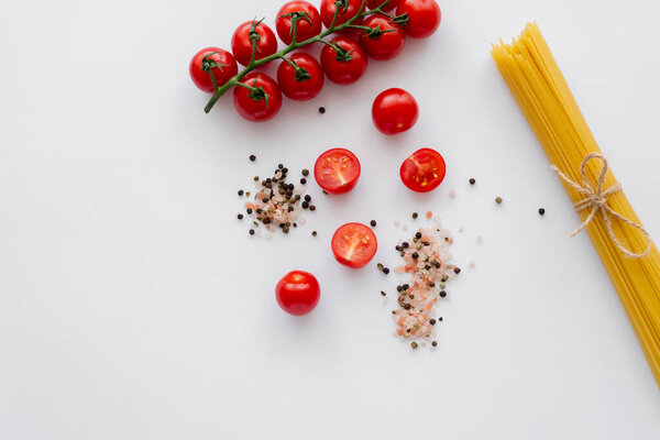 Top view of raw cherry tomatoes near spices and macaroni on white background 