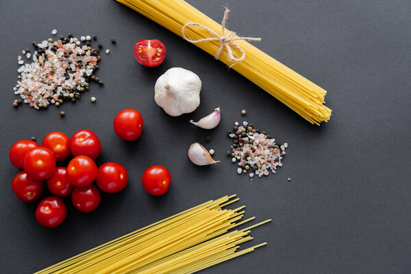 Вид сверху сырых овощей рядом со специями и спагетти на черной поверхности 