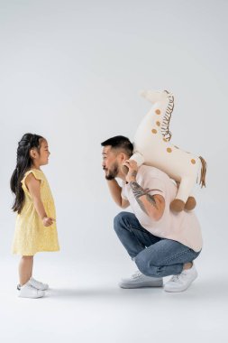 Anaokulu kızının yanında oyuncak zürafa tutan dövmeli bir Asyalı var. 