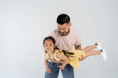 Mutlu Asyalı adam kollarında, sarı elbiseli, neşeli kız çocuğu, gri renkte izole edilmiş.