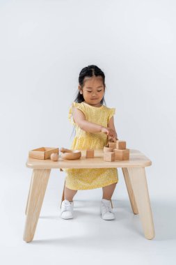 Asyalı bir çocuğun gri masada tahta oyuncaklarla oynaması.