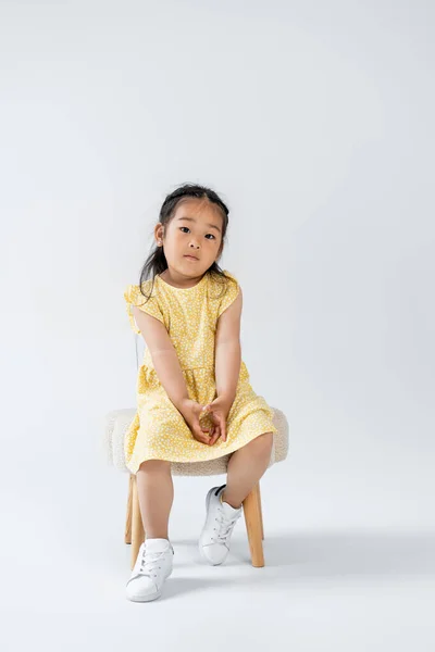 黄色のドレスを着たアジア系の子供とグレーの椅子に座っている白いスニーカー — ストック写真