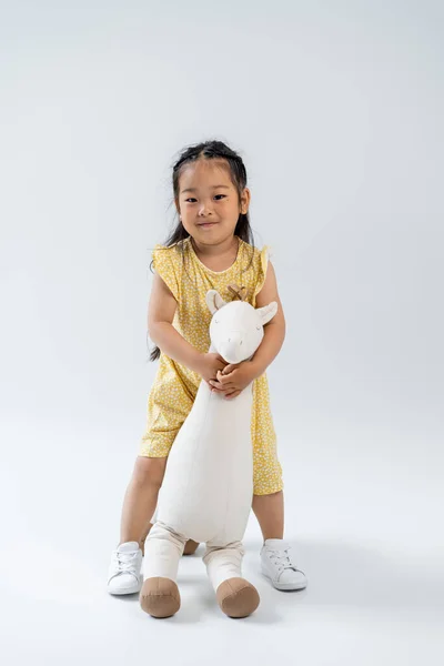 Full Length Happy Asian Kid Holding Toy Giraffe Standing Grey — Stock Photo, Image