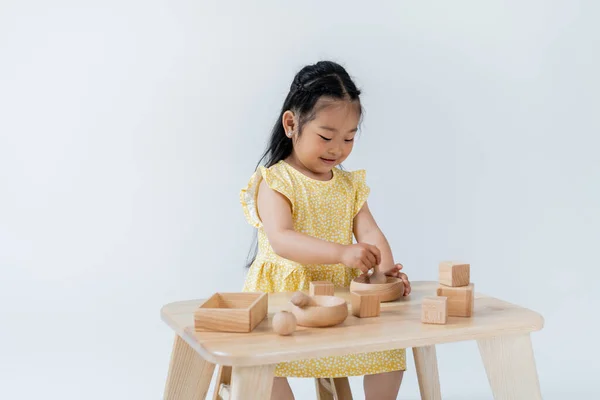 Счастливая Азиатская Девушка Держит Деревянную Ложку Возле Чаши Играя Изолированно — стоковое фото