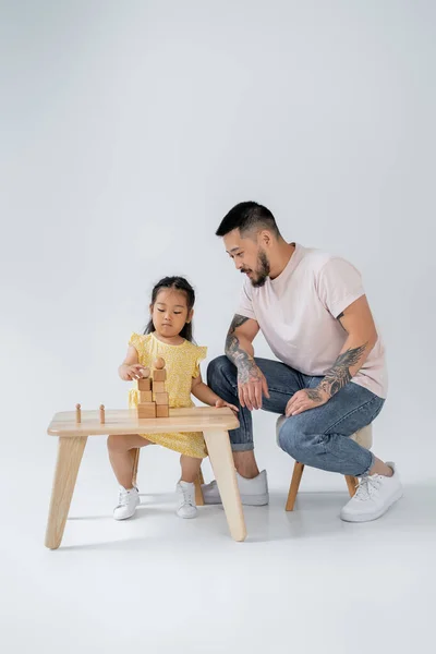 Tätowierte Asiatische Mann Blick Auf Brünette Tochter Spielen Mit Holzspielzeug — Stockfoto