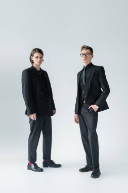 Gri arka planda kameraya bakan tam boy eşcinsel çift. 