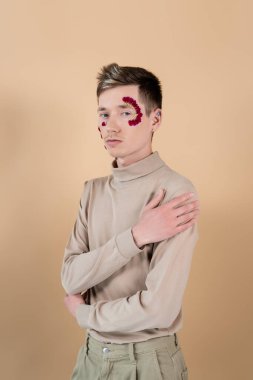 Yüzünde taç yaprakları olan bir adam bej rengi kameraya bakıyor. 