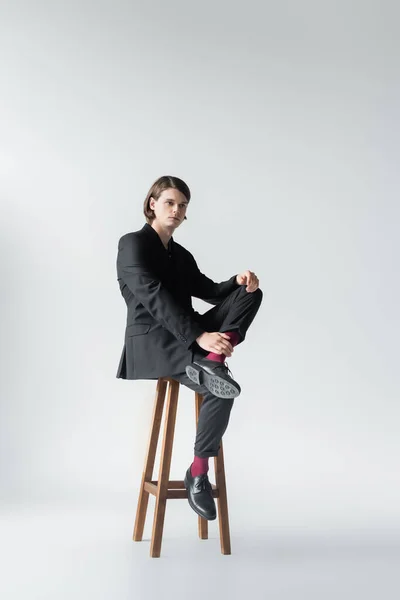 灰色の背景に椅子に座っているスタイリッシュな男の完全な長さ — ストック写真