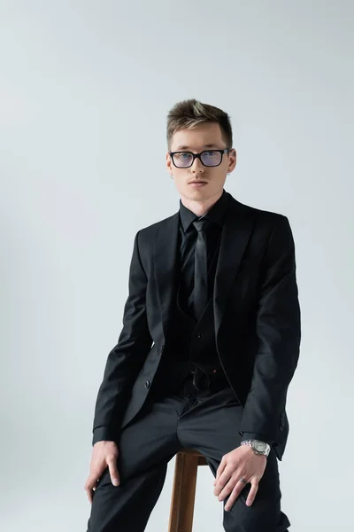 Ung Man Formell Klädsel Glasögon Sitter Stol Isolerad Grå — Stockfoto