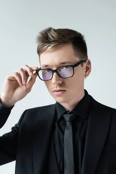 Portrait of young man i formal wear holding eyeglasses looking at camera isolated on grey