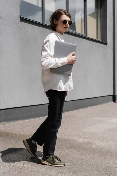Молодий Чоловік Сонцезахисних Окулярах Тримає Ноутбук Біля Будівлі Міській Вулиці — стокове фото