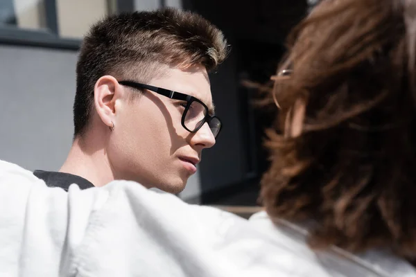 Young man in eyeglasses looking at blurred boyfriend on urban street