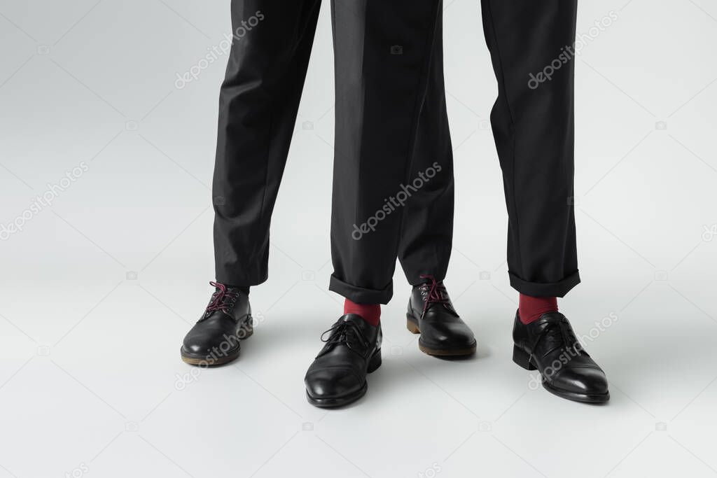 Cropped view of gay couple in shoes standing on grey background 