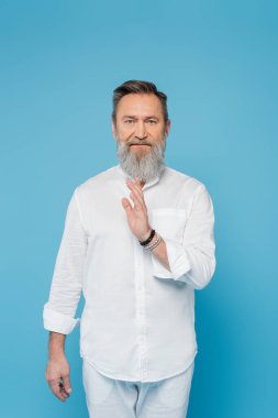 Gri sakallı kıdemli guru adam mavi üzerine izole edilmiş kutsama hareketi gösteriyor.